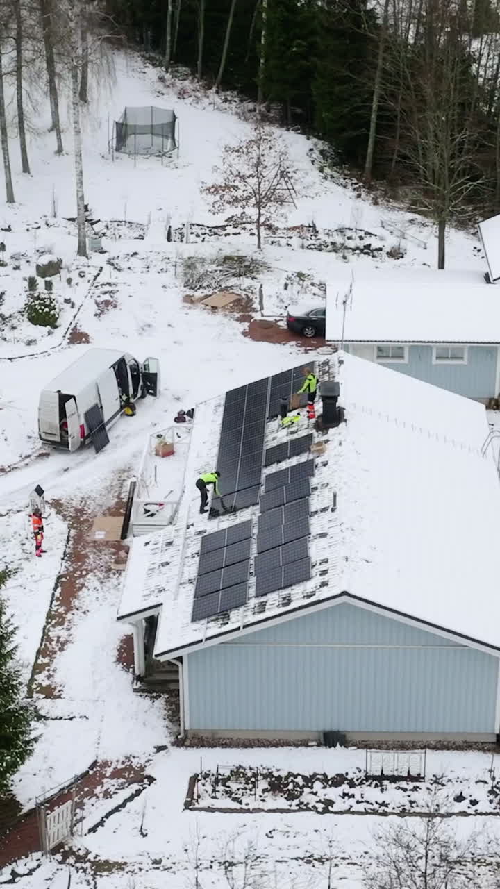 Aerial view around workers installing solar panels on a house roof, winter day