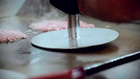 4k imágenes cinematográficas de cocina de comida de un chef preparando y haciendo una deliciosa hamburguesa casera en la cocina de un restaurante en cámara lenta aplastando la carne en hamburguesas aplastadas en la parrilla