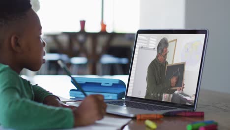 niño afroamericano sentado en un escritorio usando una computadora portátil teniendo una lección escolar en línea