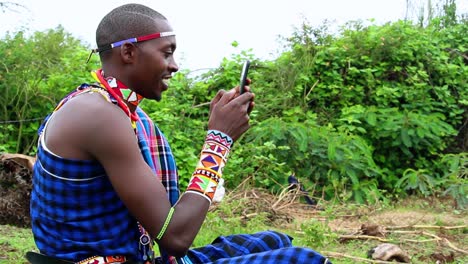 glad masai male chilling and texting with his girlfriend, in wild african nature