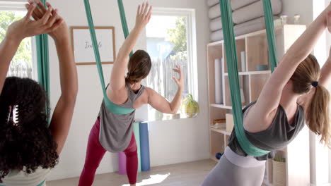 focused diverse fitness teenage girls in aerial yoga class in big white room, slow motion