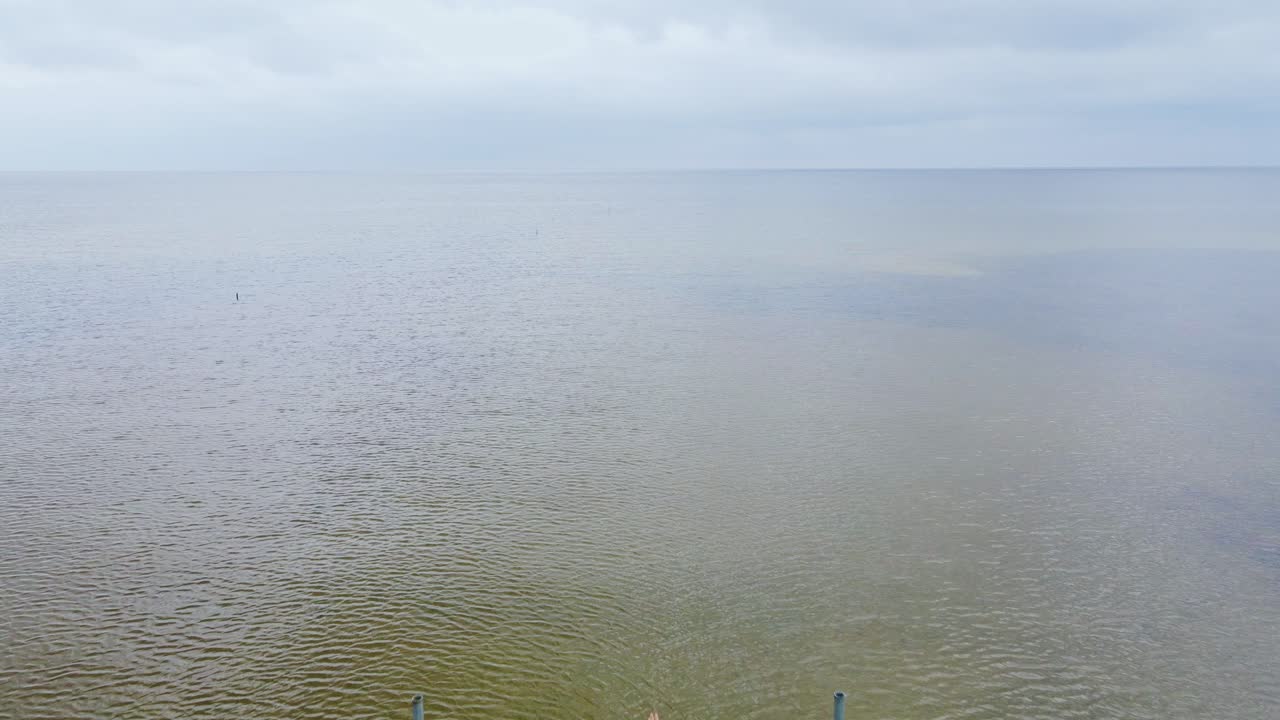 Two cyclists pause at wooden pier's edge looking out over moody Baltic Sea