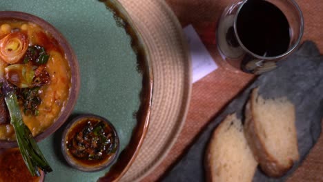 overhead shot of a table with a glass of wine, slices of bread and a turntable with casseroles with homemade food and locro