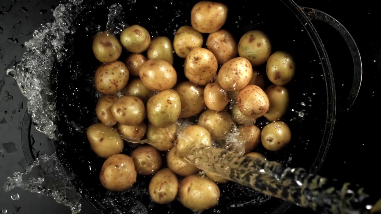 Vann som spruter i sakte film på ferske poteter i en gryte