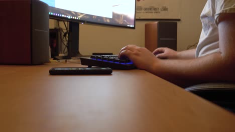 man typing at his desktop gaming computer with blue lit keyboard and large curved screen