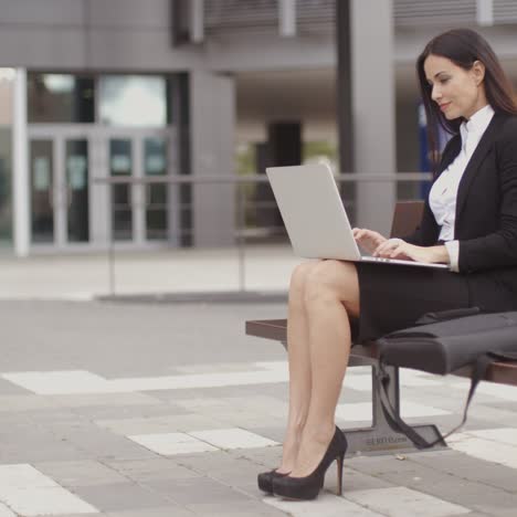 woman sitting with laptop on bench outdoors