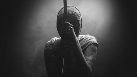a mummified woman against the dark background pose with the walking staff