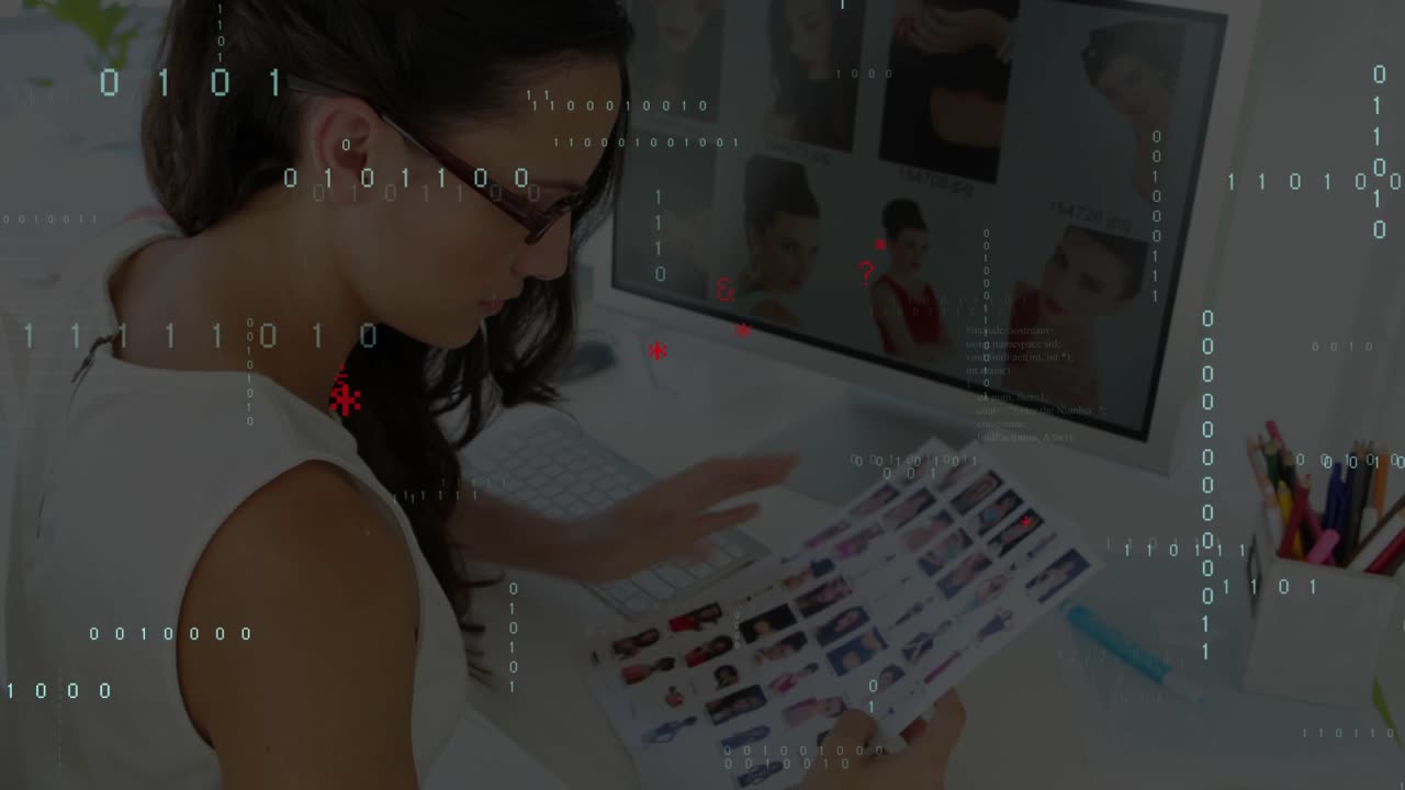 Vertical video: Comparing woman in white top picking prints at desk, monitor overlaying data grids