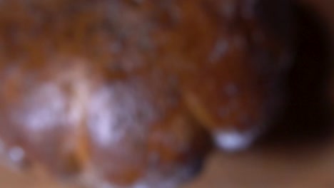 Flower-shaped-fennel-seed-bread-with-golden-baked-crust-falling-down-on-wooden-chopping-board-while-going-out-of-focus,-SLOW-MOTION