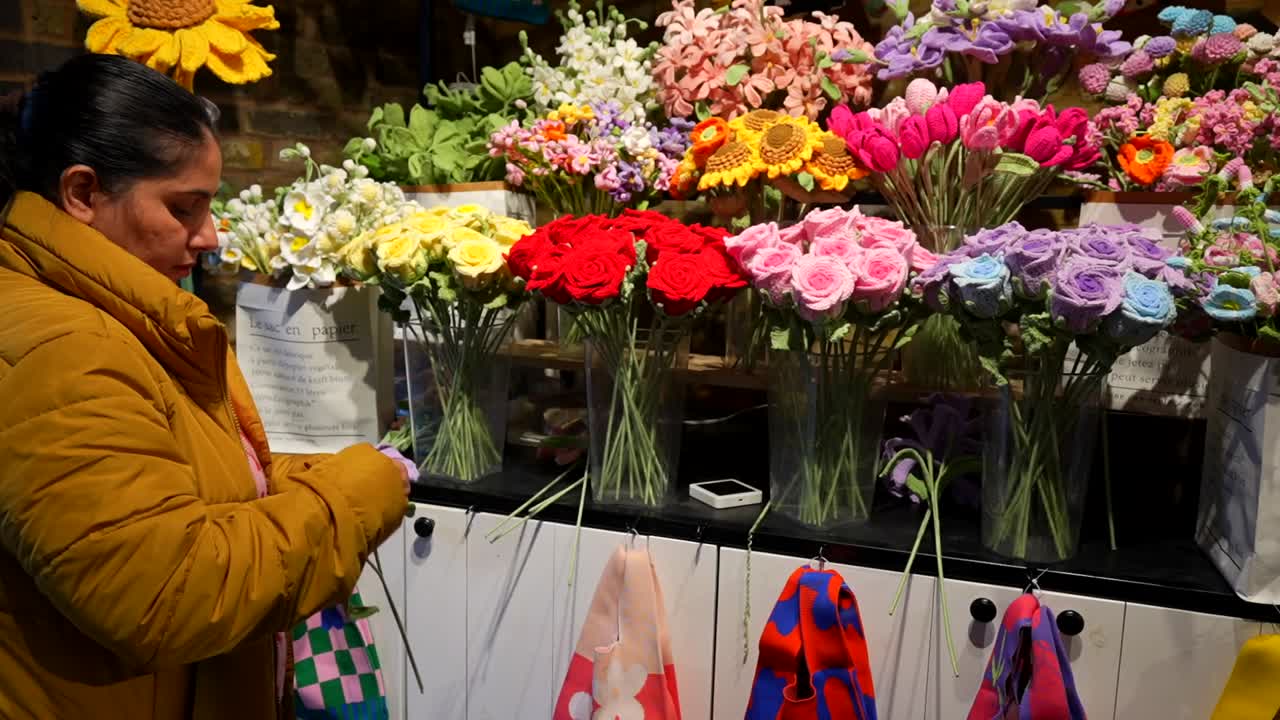 Woman crafting colorful fabric flowers at a vibrant floral stand in Camden Market, London