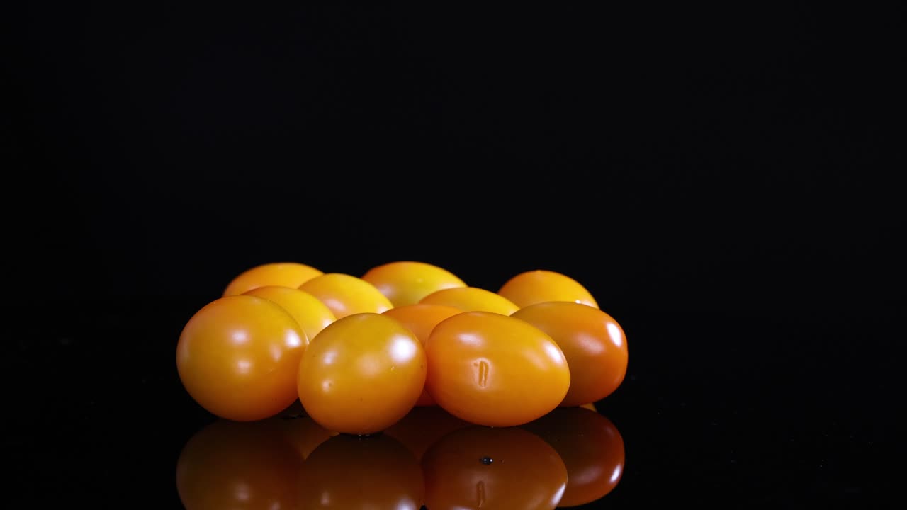 Yellow tomatoes rotate on a glossy black surface under bright lighting, creating a dynamic visual effect
