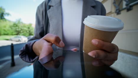 woman using tablet outdoors while holding coffee