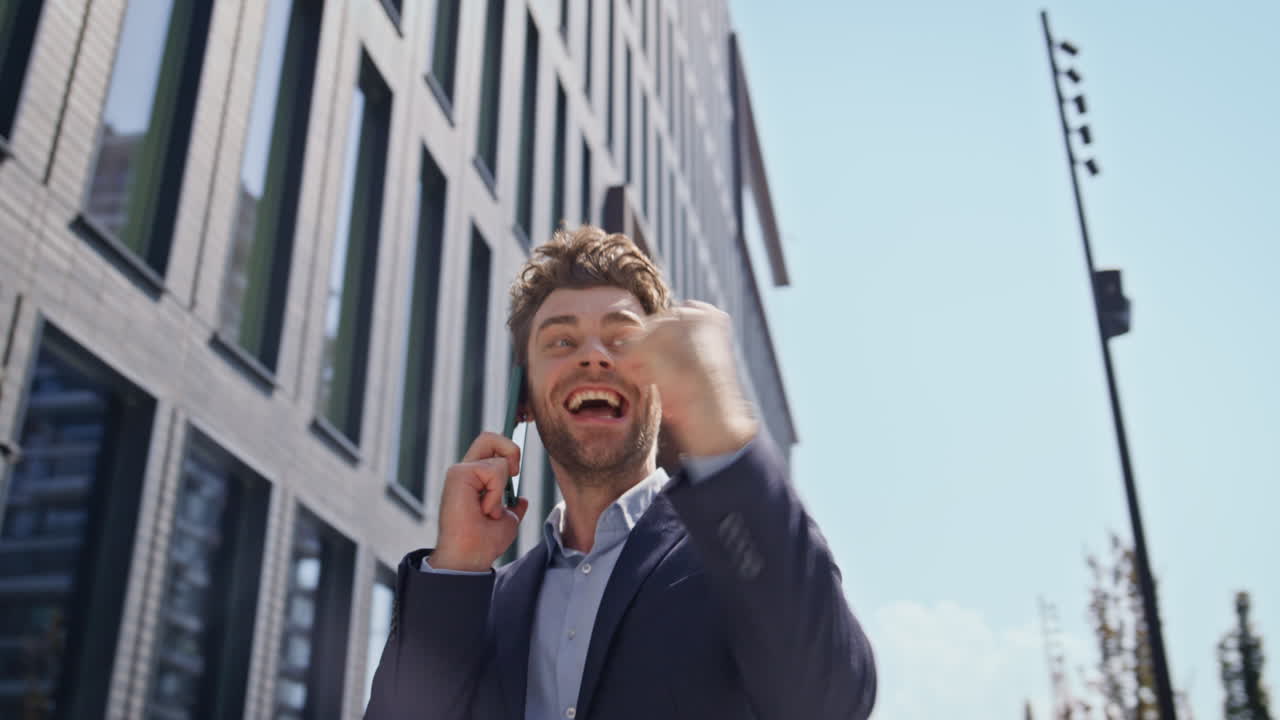 hombre emocionado riendo llamada de teléfono inteligente caminando área de negocios soleada de cerca.