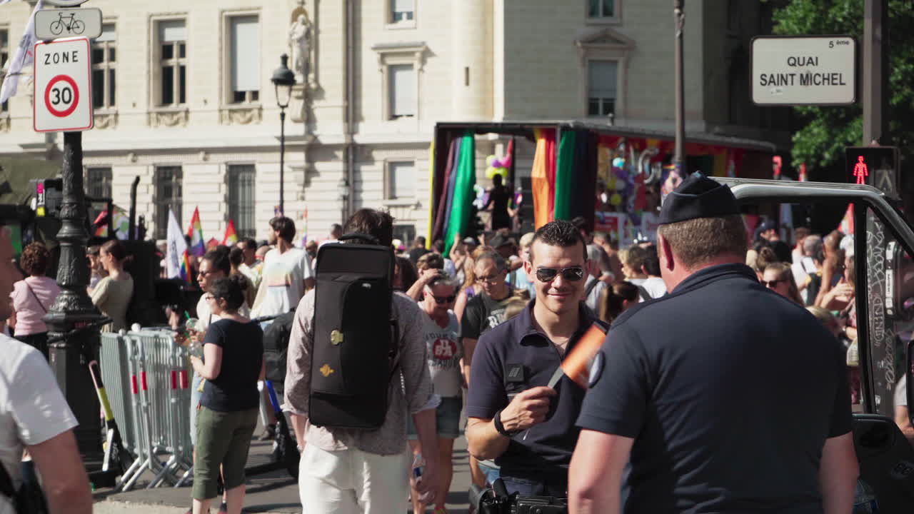 Policemen on duty at the Gay Pride march watching the people pass by and his partner waving a rainbow flag.