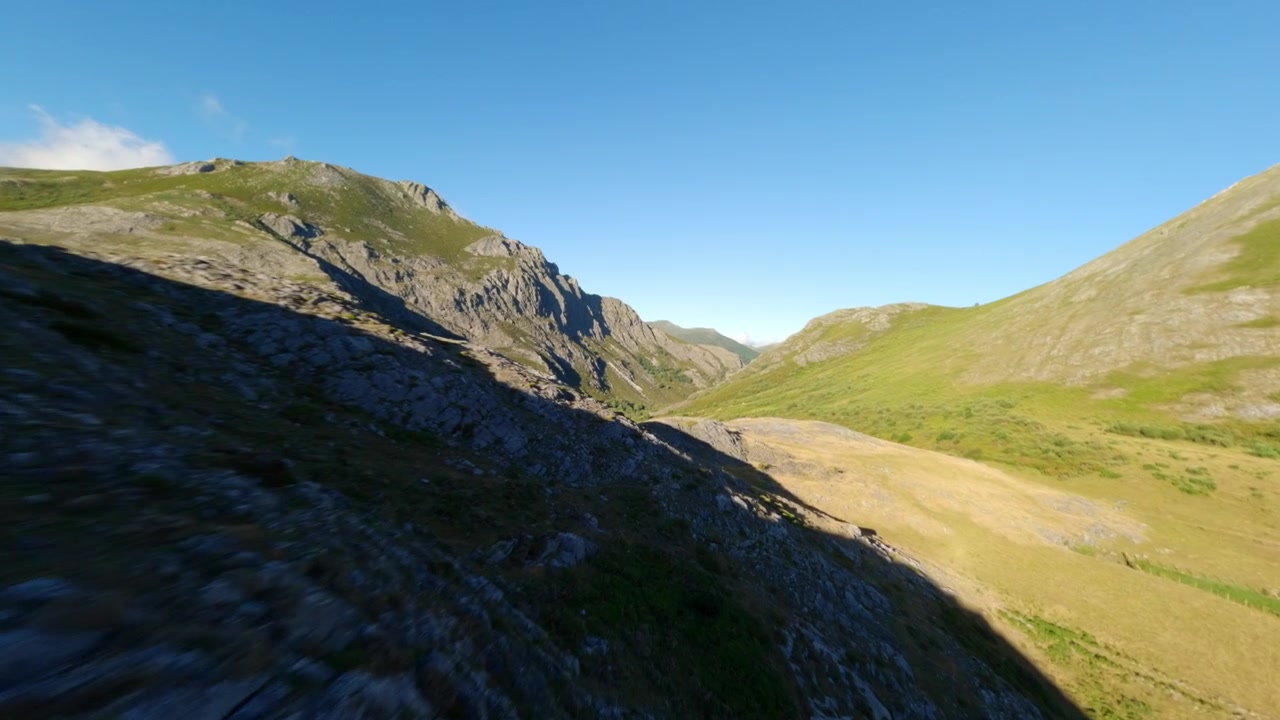 Volo dinamico di drone FPV che cattura la bellezza aspra delle montagne di León e un lago alpino incontaminato sotto un cielo azzurro limpido. Ideale per contenuti di viaggio e sostenibilità.