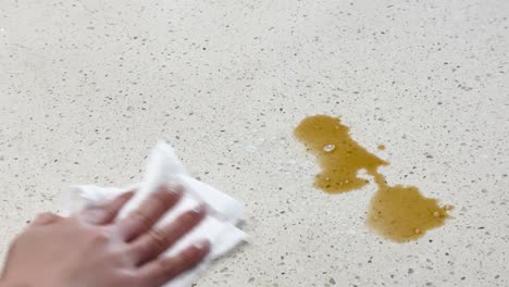a hand wipes coffee spill on a light countertop using a paper towel, demonstrating effective cleaning technique