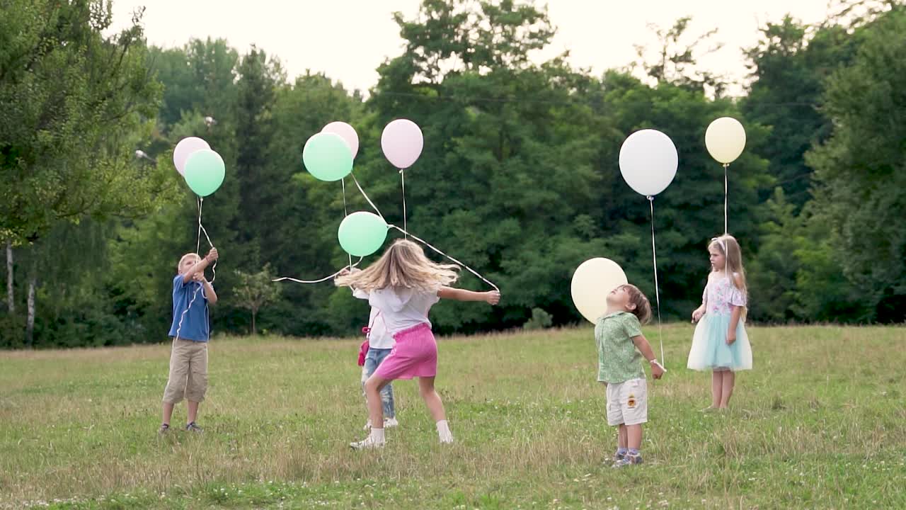 Children in the summer park on the grass play with balloons. Rest of boys and girls in nature near the forest. Slow motion