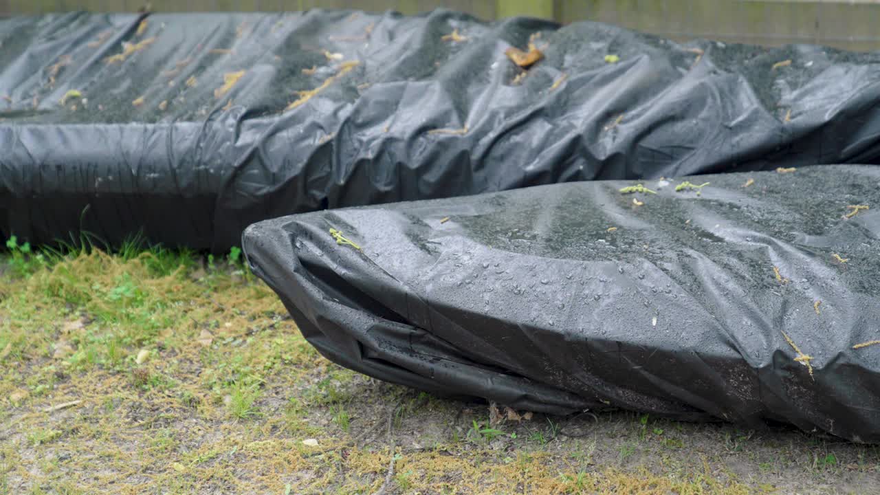 Two covered kayaks sitting in the rain.