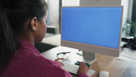 vista trasera de una mujer de raza mixta trabajando en una computadora en una pantalla azul
