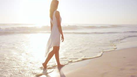 Hermosa-Mujer-Con-Vestido-Blanco-Caminando-Por-La-Playa-Al-Atardecer-En-Cámara-Lenta-Dragón-Rojo