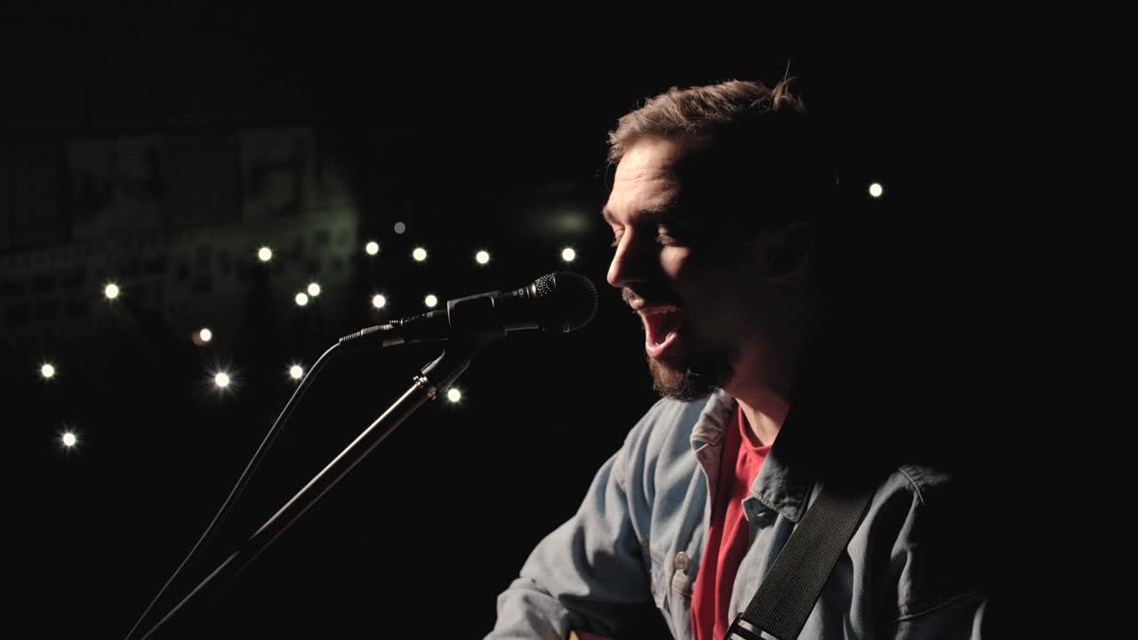 한 뮤지션이 큰 무대에서 기타를 연주하고 있으며, 관객들은 배경에 불을 들고 있습니다. 관객실은 아름다운 박이는 불빛으로 가득 차 있습니다.