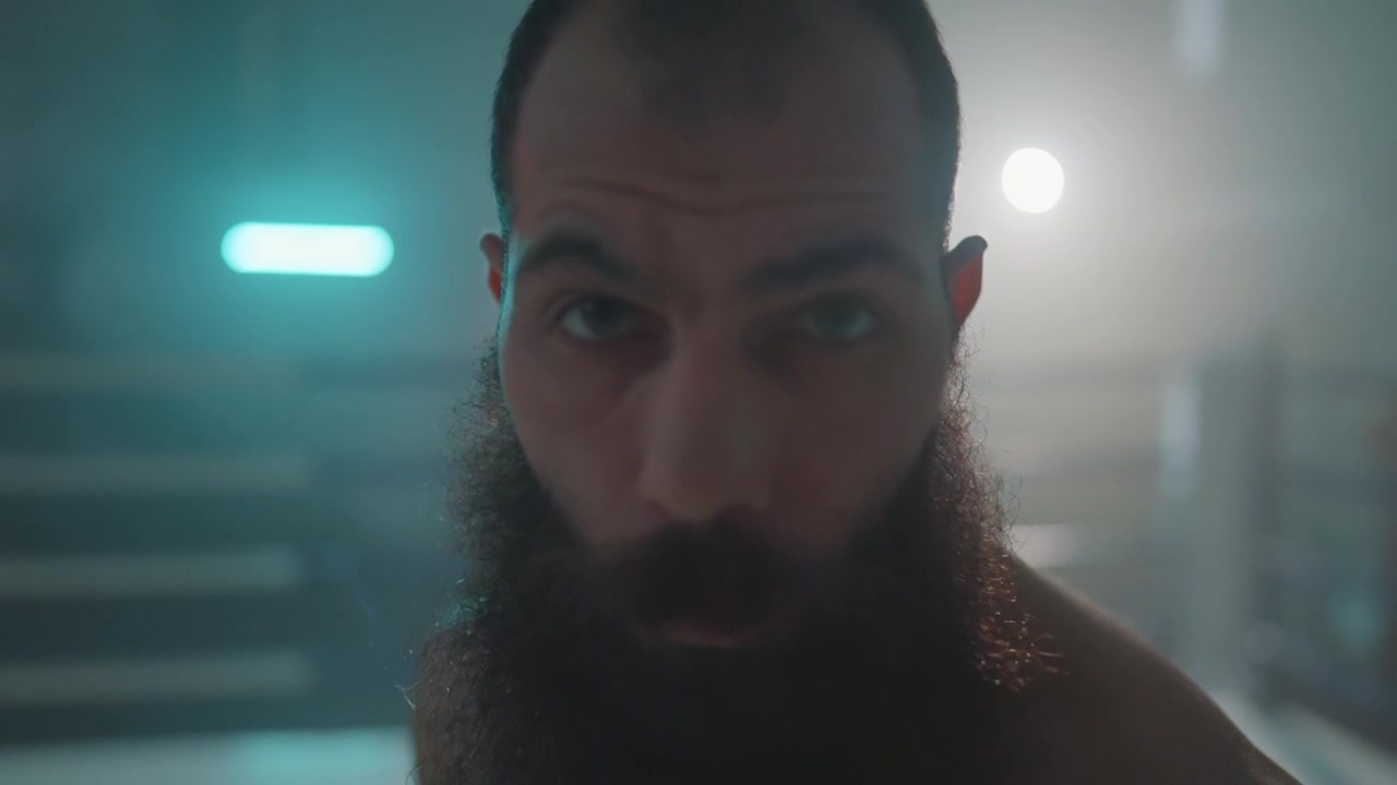 Combattente barbuto dallo sguardo intenso che fissa la telecamera in un ring da boxe