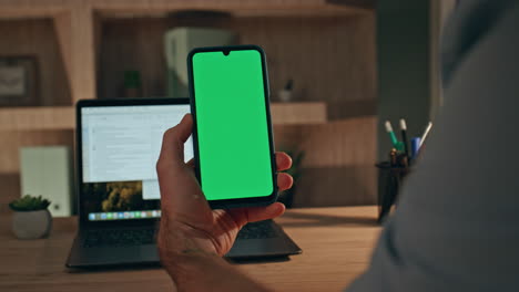 freelancer hand holding greenscreen mobile phone at office workplace close up.