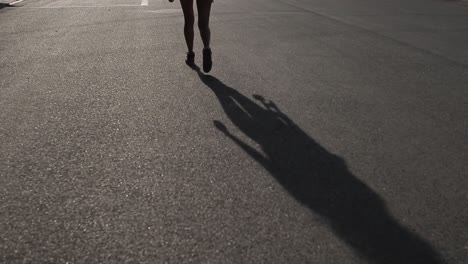sombra de asfalto de una chica caminando con patineta en la mano en el camino.
