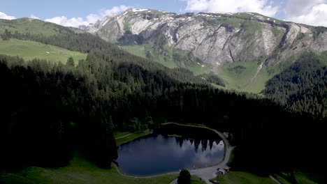 Aerial-approach-French-Alps-pine-tree-landscape-with-clouds-in-blue-sky-above-mountain-rocks-at-Lac-du-Mines-d'Or-[translation:-Lake-of-Gold-Mines]-Tour-de-France-vacation-outdoor-sports-during-summer