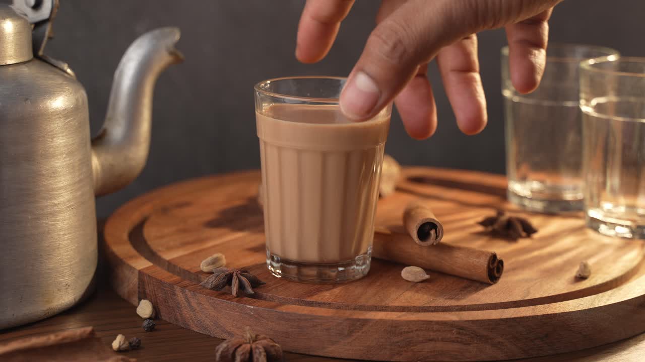 Chai indiano servito in tazze di vetro, preparato in un bollitore di metallo con masala aromatici e prelevato a mano