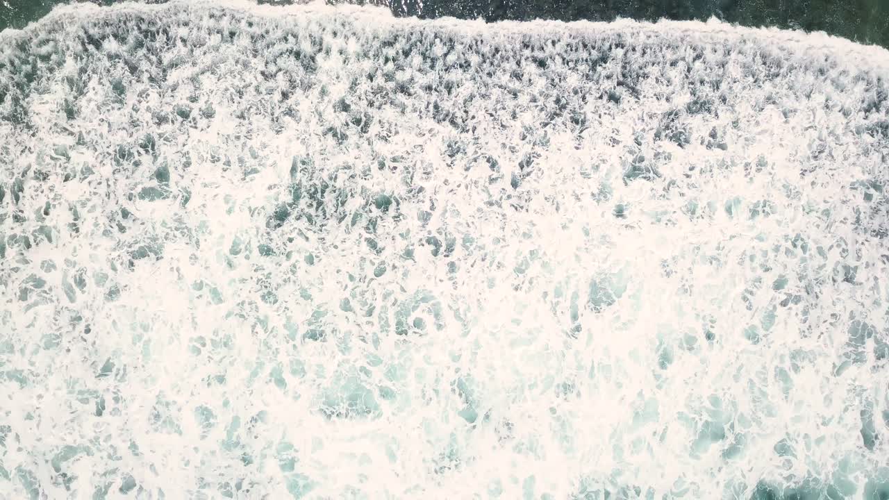 toma aérea de arriba hacia abajo de grandes olas con espuma blanca rompiendo a lo largo de la costa bajo el sol