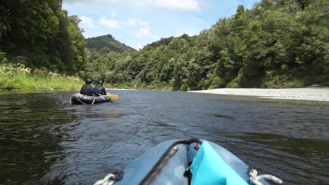 Two-people-paddle-canoes-beautiful-blue-pristine-clear-Pelorus-river,-New-Zealand-with-native-lush-forrest-in-background