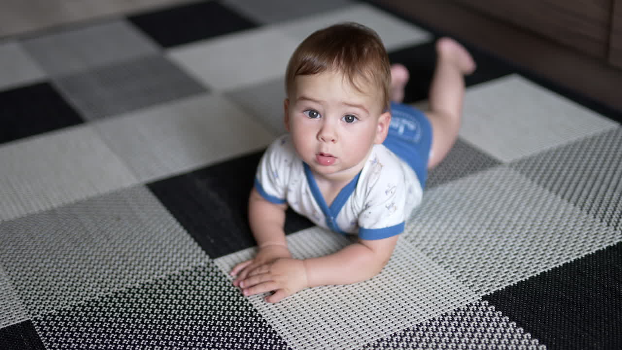 Adorable baby boy lying on the floor. Calm child looking up lying peacefully on the belly trying to crawl. Close up.