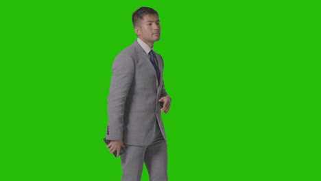 three quarter length studio shot of businessman in suit looking at mobile phone against green screen 1