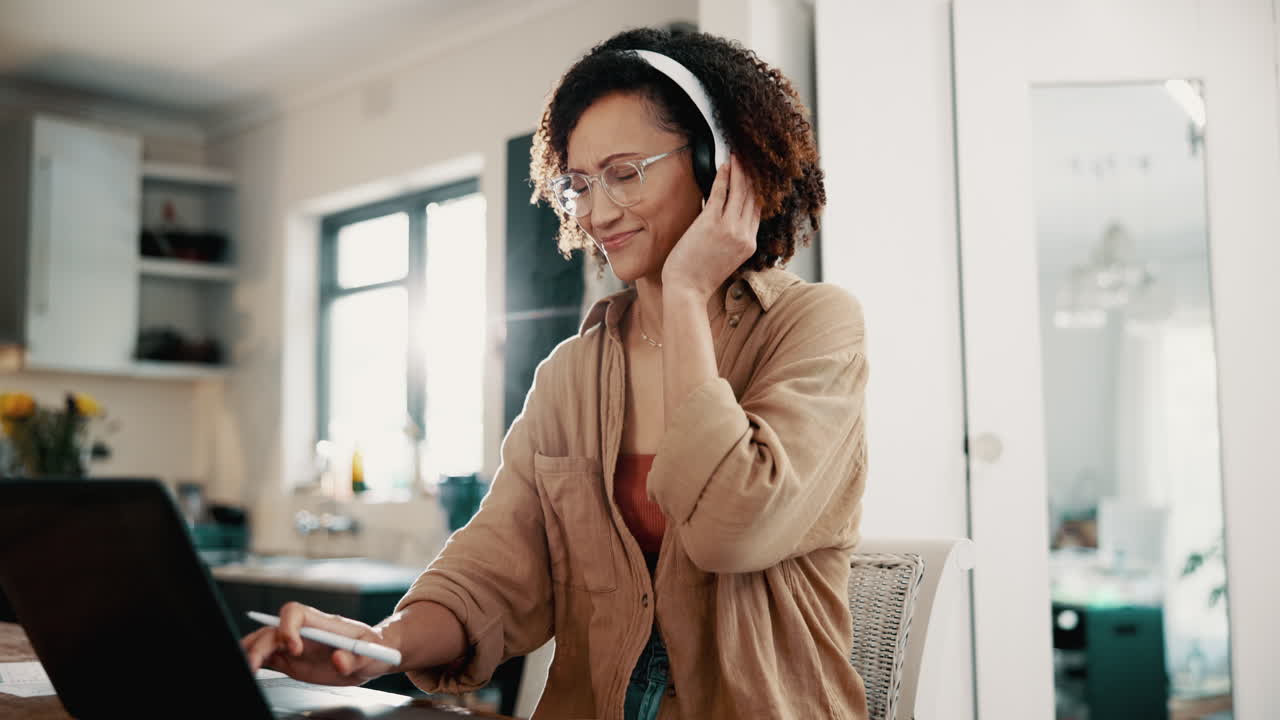 Smiling woman working on her laptop at home, listening to music with headphones