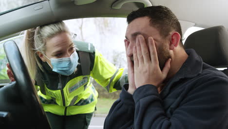 Female-Paramedic-Wearing-Face-Mask-Helping-Injured-Male-Driver-Involved-In-Road-Traffic-Accident