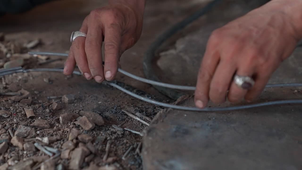 Hands working with cables on a dusty ground, focus on manual labor and craftsmanship