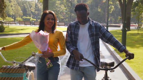 pareja caminando por el parque con bicicletas y flores