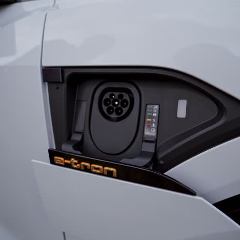 charging detail of white audi e-tron. hand pressing the button to open the charger of an electric vehicle. automatic door opening and closing to reveal the charging hub.