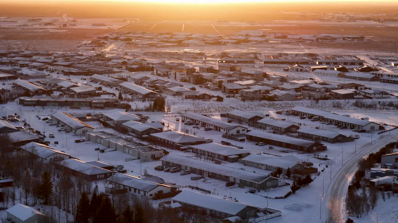 воздушное видео беспилотника, смотрящее над покрытыми снегом зданиями, когда яркое солнце встает на горизонте, бросая красивое золотое свечение на ландшафт