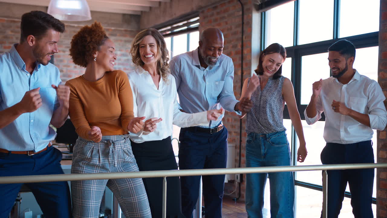 Forretningsteam fejrer til møde på multikulturelt kontor, med kolleger der danser og hygger sig