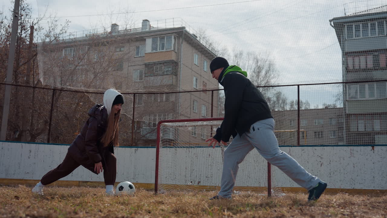 골대 근처에서 선수들이 경쟁하는 모습, 선수와 배경이 있는 경기 장면, 경기장에서 운동선수 간의 극적인 순간, 도시 환경과 집중된 분위기 속에서 마른 잔디 위에서 펼쳐지는 경쟁적인 장면