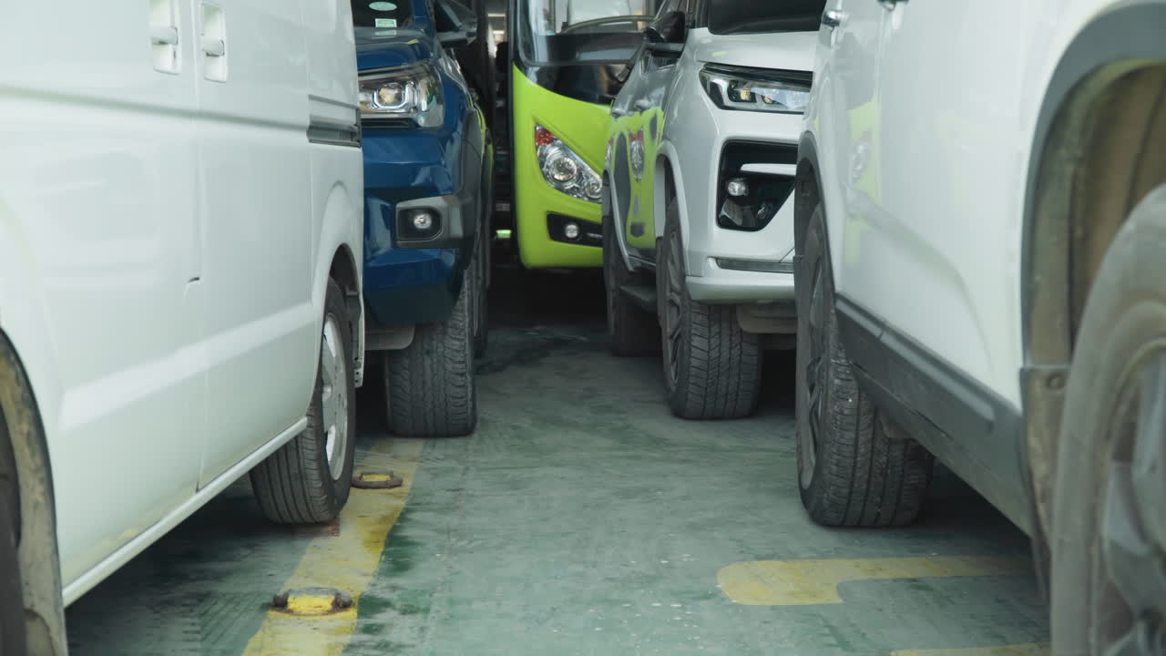 Tight parking between white delivery vans, narrow alley with green truck front visible, worn curb markings, dirty tires and close vehicle alignment conveying logistical stress in industrial lot
