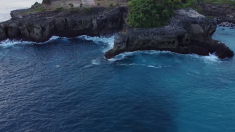 nusa ceningan's blue lagoon along the coastal cliffs with ocean waves from an aerial drone, indonesia