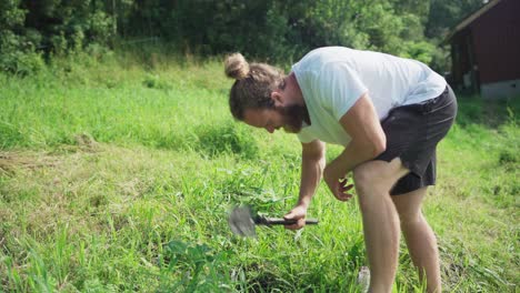 A-Man-Using-A-Mini-Garden-Shovel-Digging-On-A-Grassy-Ground