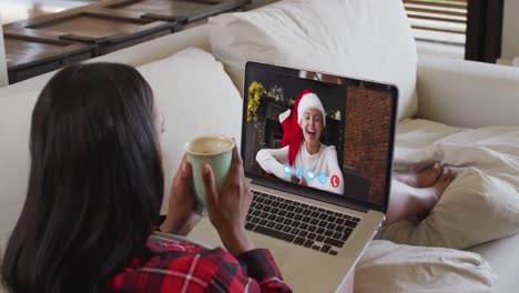 Mixed-race-woman-using-laptop-on-video-chat-with-woman-during-christmas-at-home