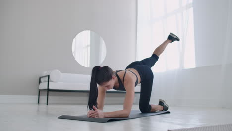 home exercises for a beautiful body. a slender brunette in sportswear is lifting her legs back while standing on all fours on the rug