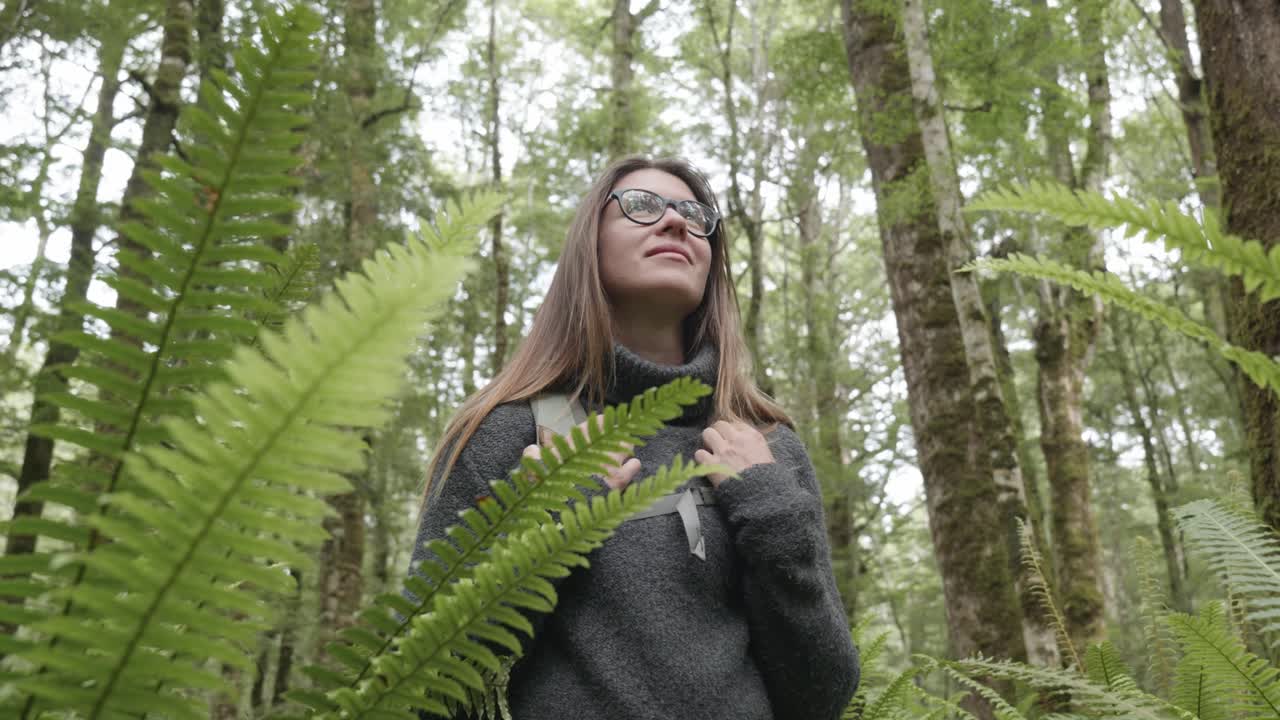 주변을 둘러보는 숲에서 페른 사이에 안경을 가진 젊은 백인 여성