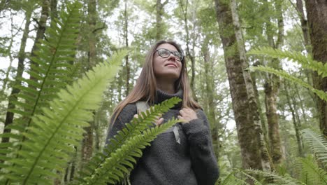 Junge-Kaukasische-Frau-Mit-Brille-Zwischen-Farnen-In-Einem-Wald,-Die-Sich-Umschaut