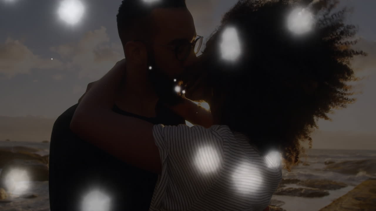 animación de puntos de luz sobre una pareja biracial besándose en la orilla del mar